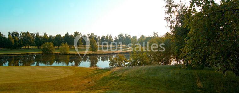 Paysage avec un lac bordé d'arbres, une pelouse bien entretenue et un ciel clair en arrière-plan.