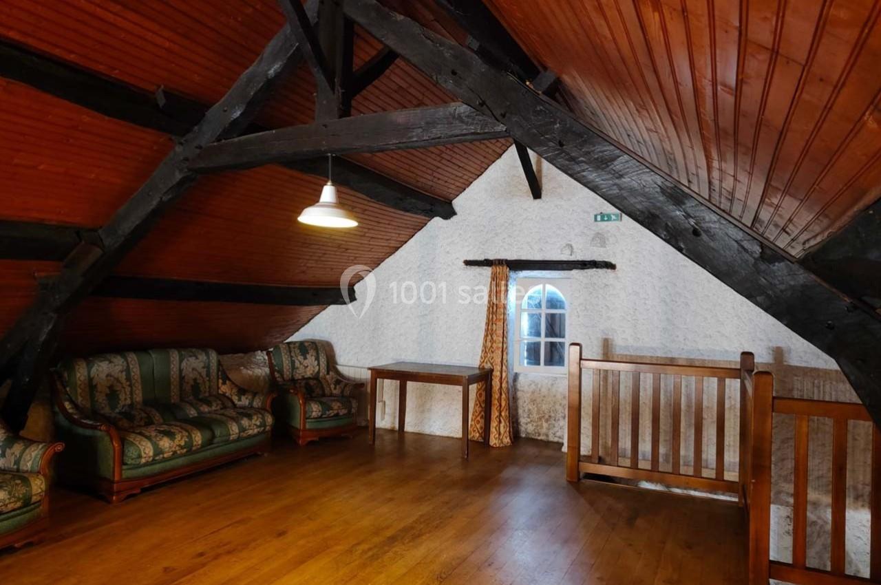 Grenier aménagé avec parquet, poutres apparentes, canapé, table en bois, fenêtre et garde-corps en bois.