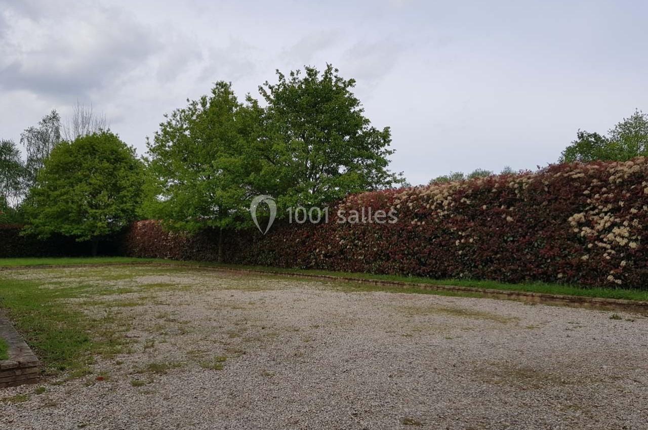 Allée en gravier bordée d'une haie fleurie et d'arbres verts sous un ciel légèrement nuageux.