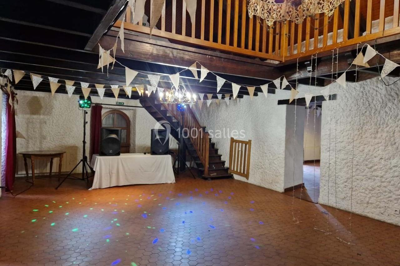 Salle de réception avec poutres apparentes, guirlandes de fanions, éclairage coloré et espace de danse.