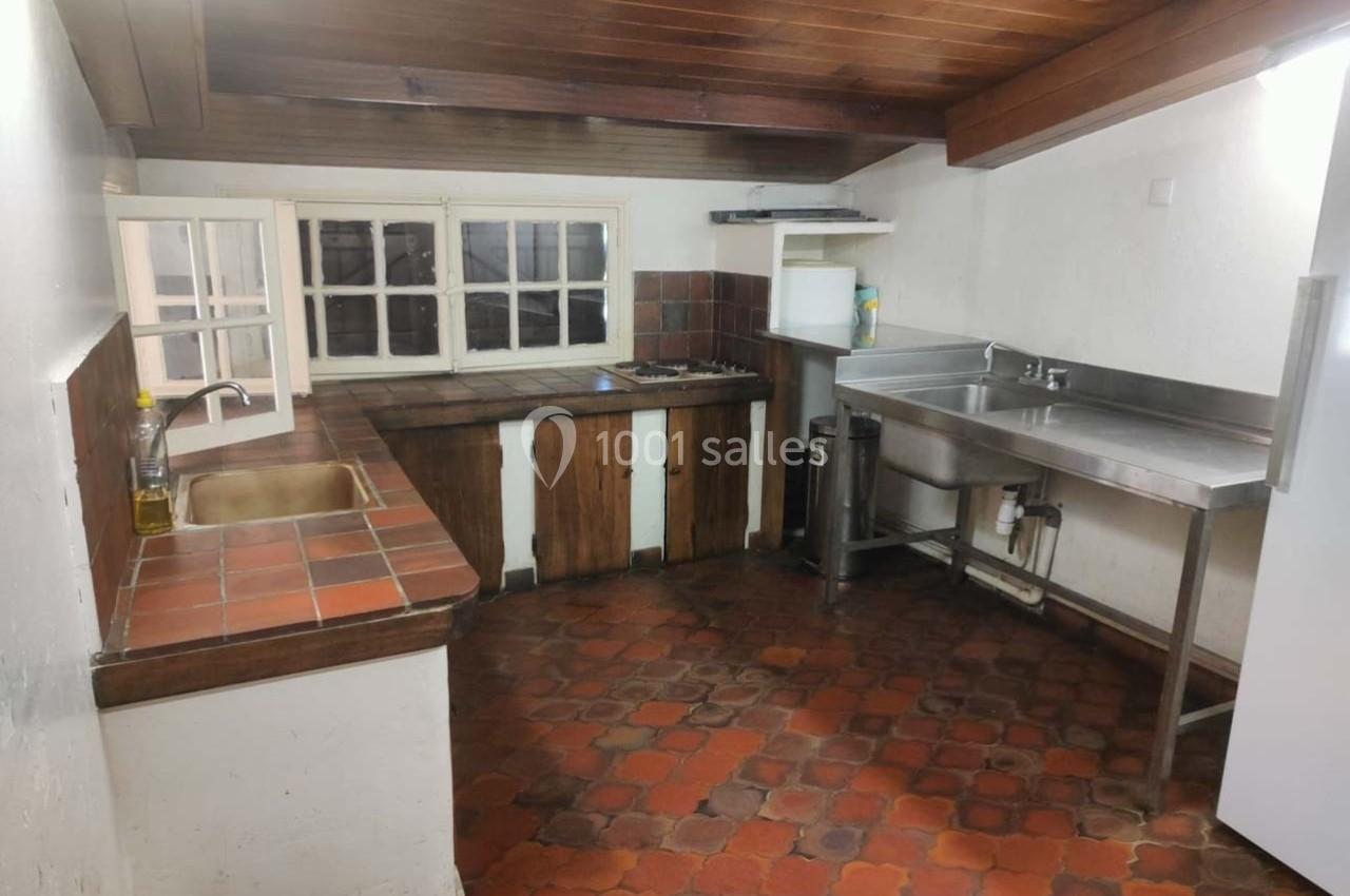 Cuisine rustique avec plan de travail en bois, évier en inox, carrelage au sol et fenêtres à petits carreaux.