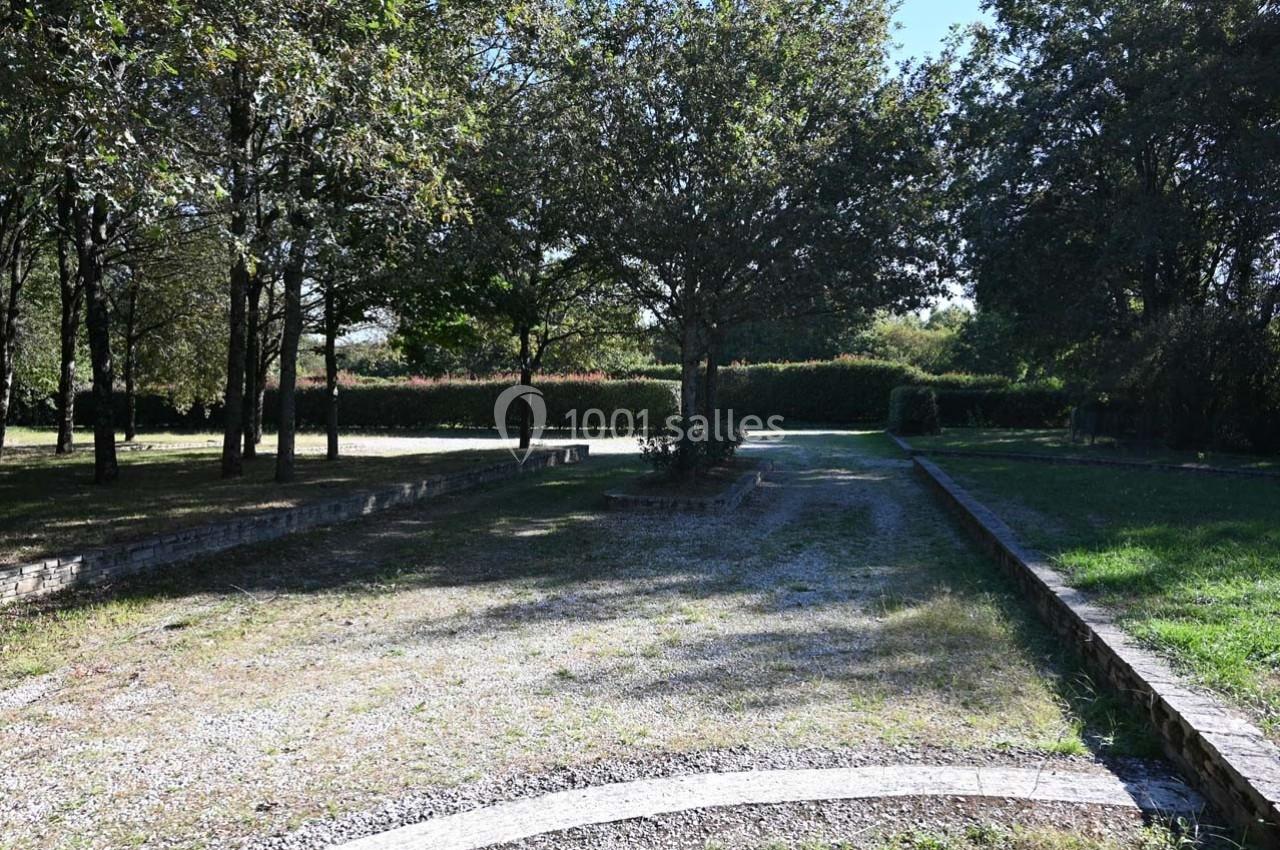 Allée gravillonnée bordée d'arbres et de haies, avec zones d'herbe et de lumière filtrant à travers le feuillage.