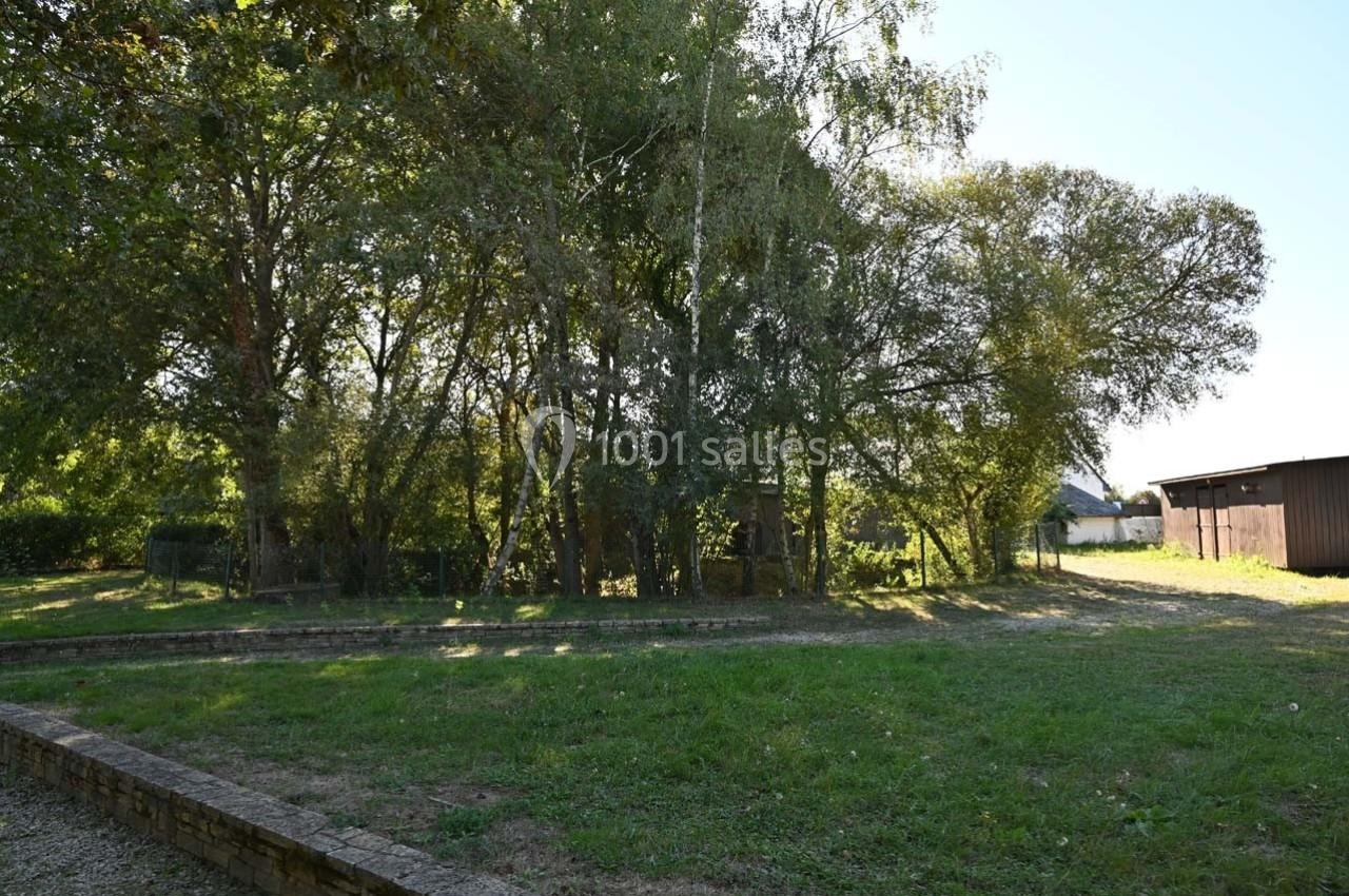 Un espace herbeux bordé d'arbres avec une cabane en bois visible à travers le feuillage.