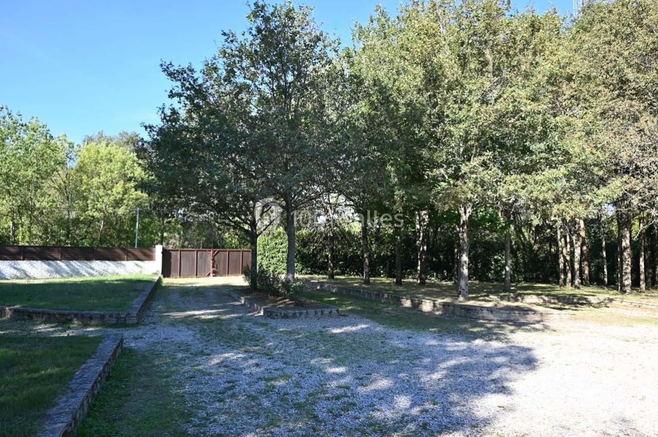 Allée gravillonnée bordée d'arbres et d'espaces verts, menant à un portail en bois fermé.