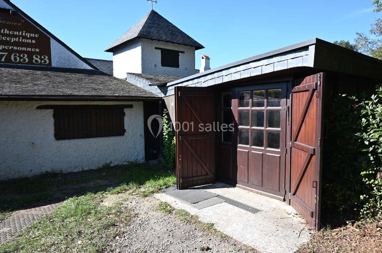 Entrée d'un bâtiment avec une porte en bois ouverte, entourée d'un mur blanc et d'une toiture en ardoise.