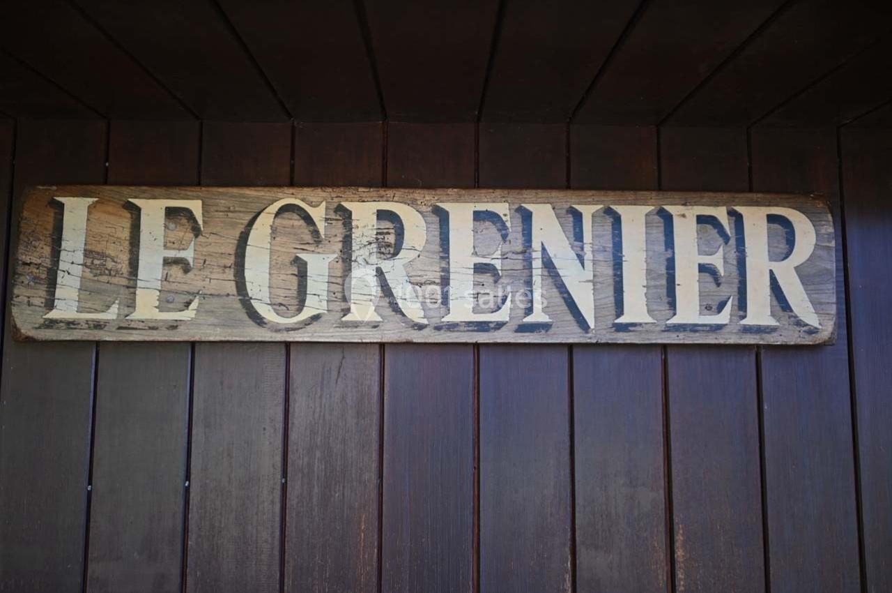 Panneau en bois vieilli avec l'inscription ’Le Grenier’ fixé sur un mur en bois sombre.