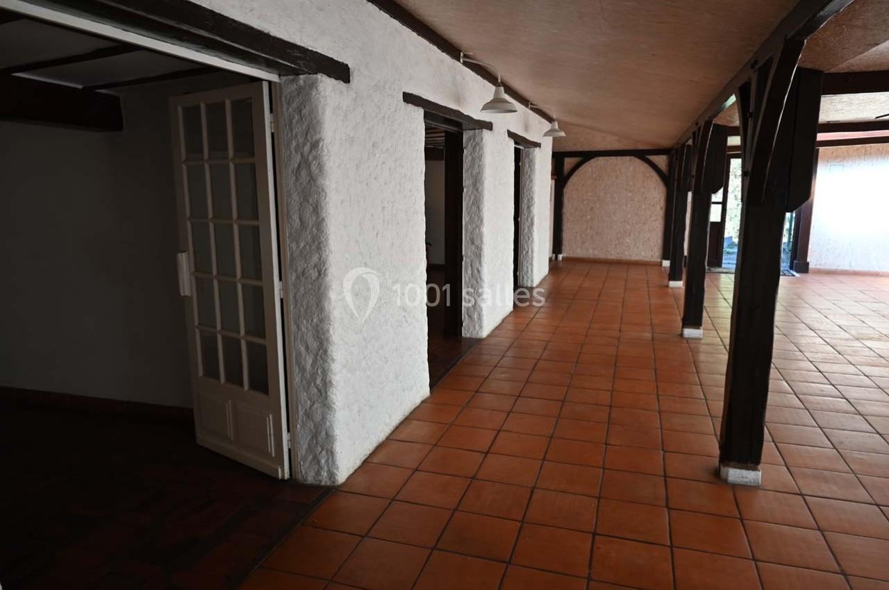 Couloir intérieur avec sol en carrelage orange, murs blancs texturés et poutres en bois sombre.