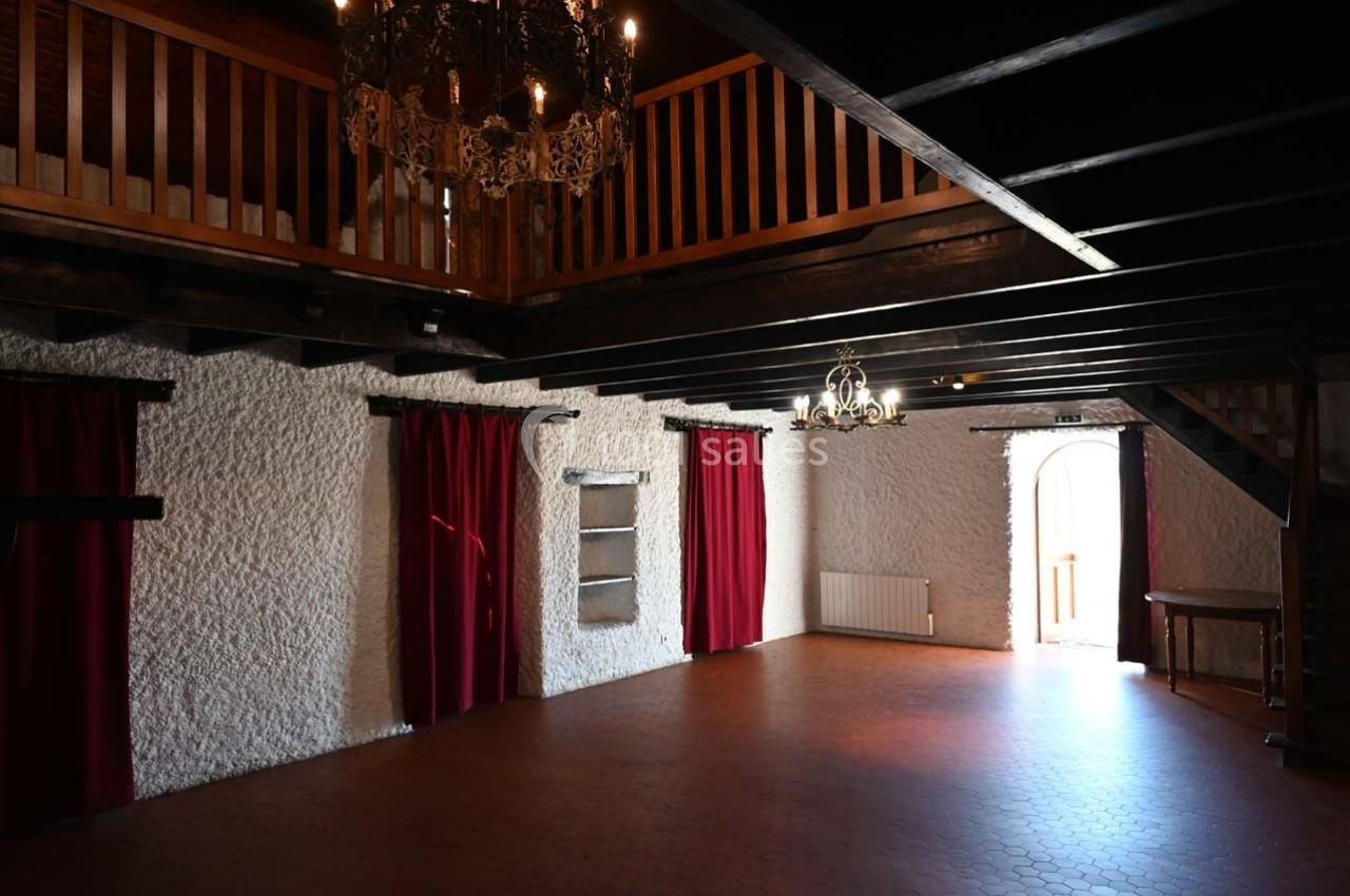 Salle intérieure avec murs en pierre blanche, rideaux rouges, poutres apparentes et lustres suspendus.