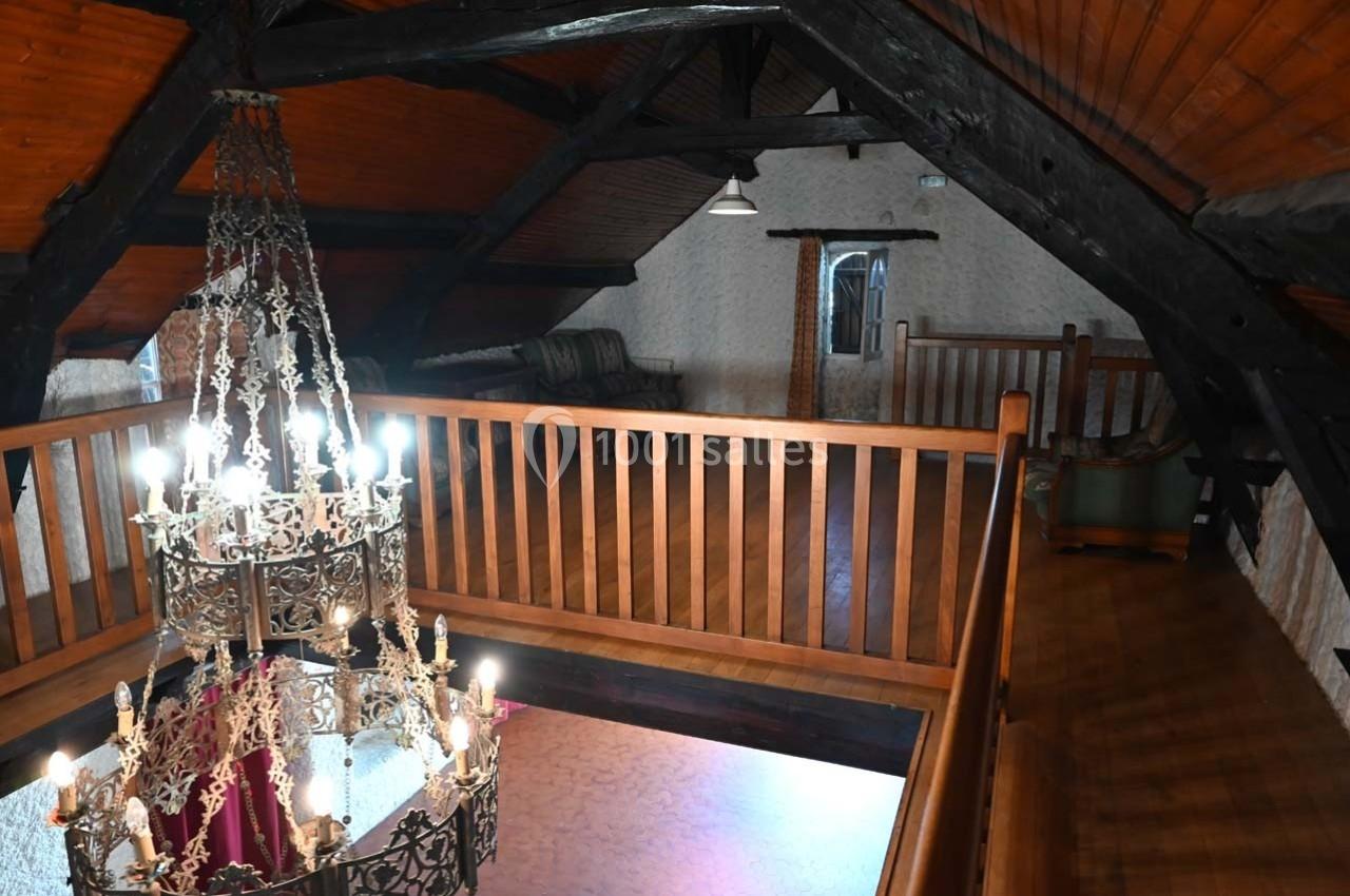 Grenier aménagé avec poutres apparentes, lustre en métal orné et balustrade en bois surplombant un espace ouvert.