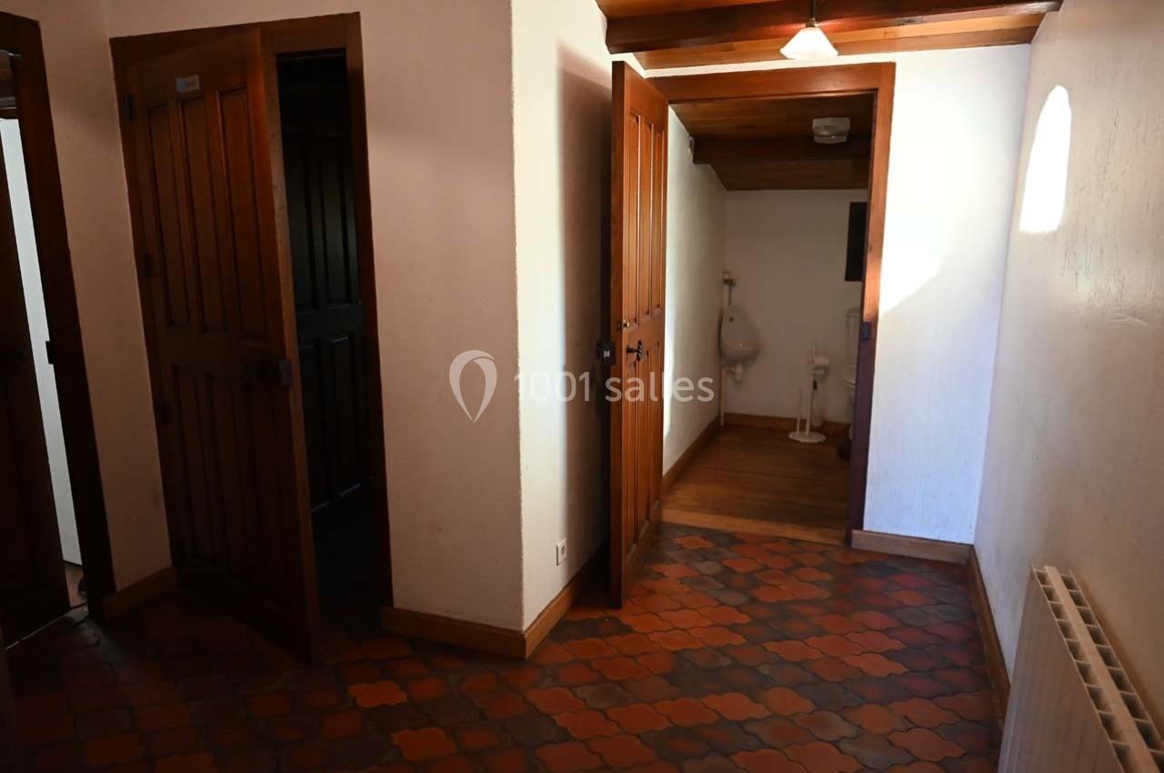 Un couloir avec des portes en bois, un sol en carreaux rouges et un accès à une pièce avec un urinoir visible.