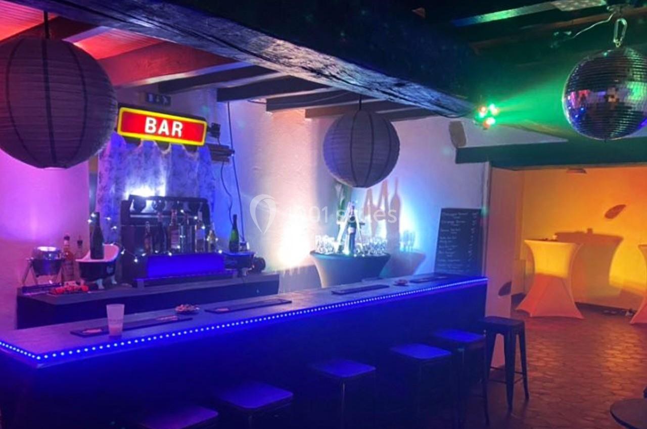 Bar éclairé par des lumières colorées avec tabourets alignés, décorations suspendues et ambiance festive.