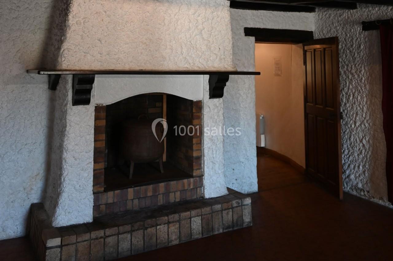 Cheminée en pierre blanche avec un chaudron en métal à l'intérieur, dans une pièce aux murs texturés et sol en carrelage.