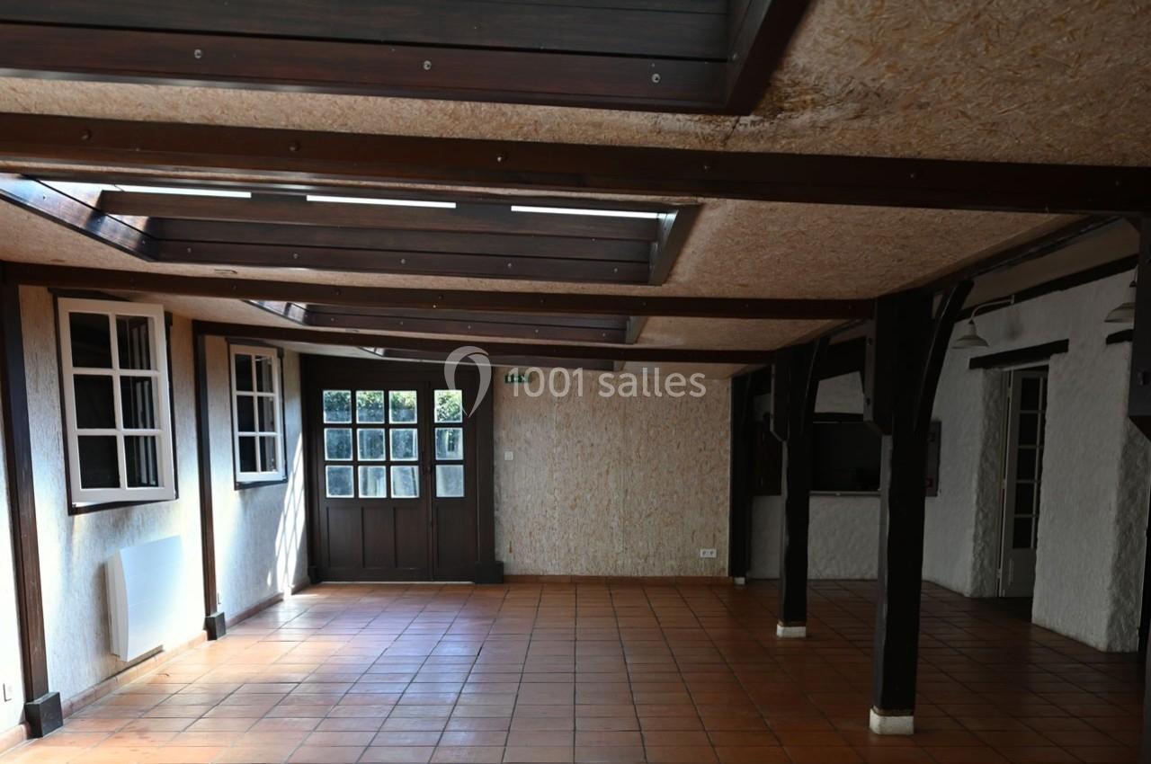 Salle vide avec carrelage orange, poutres en bois, fenêtres vitrées et puits de lumière au plafond.