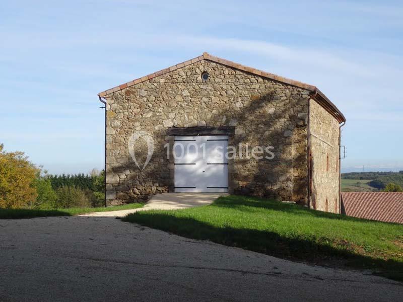 Bâtiment en pierre avec porte blanche, situé sur une colline entourée de verdure et d'un ciel dégagé.