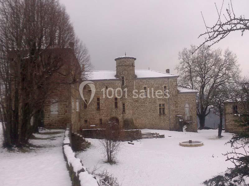 Château en pierre entouré d'arbres et de neige, avec une petite fontaine au premier plan.