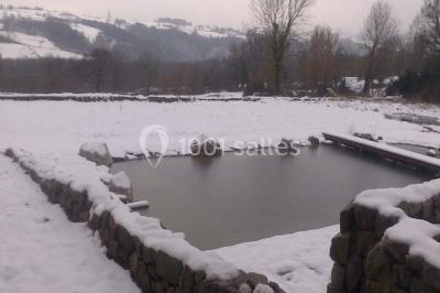 Chambre avec un lit double, draps blancs, couverture rouge, deux oreillers bleus et un mur rouge, éclairée par une fenêtre.