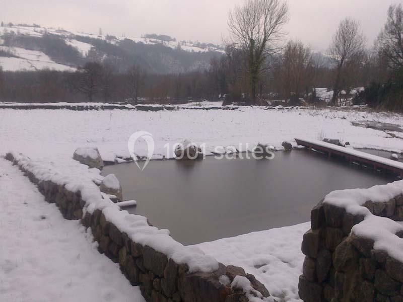Étang entouré de murs en pierre dans un paysage rural enneigé avec des collines en arrière-plan.