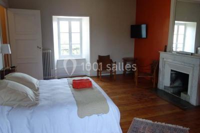 Chambre avec un lit double, draps blancs, couverture rouge, deux oreillers bleus et un mur rouge, éclairée par une fenêtre.