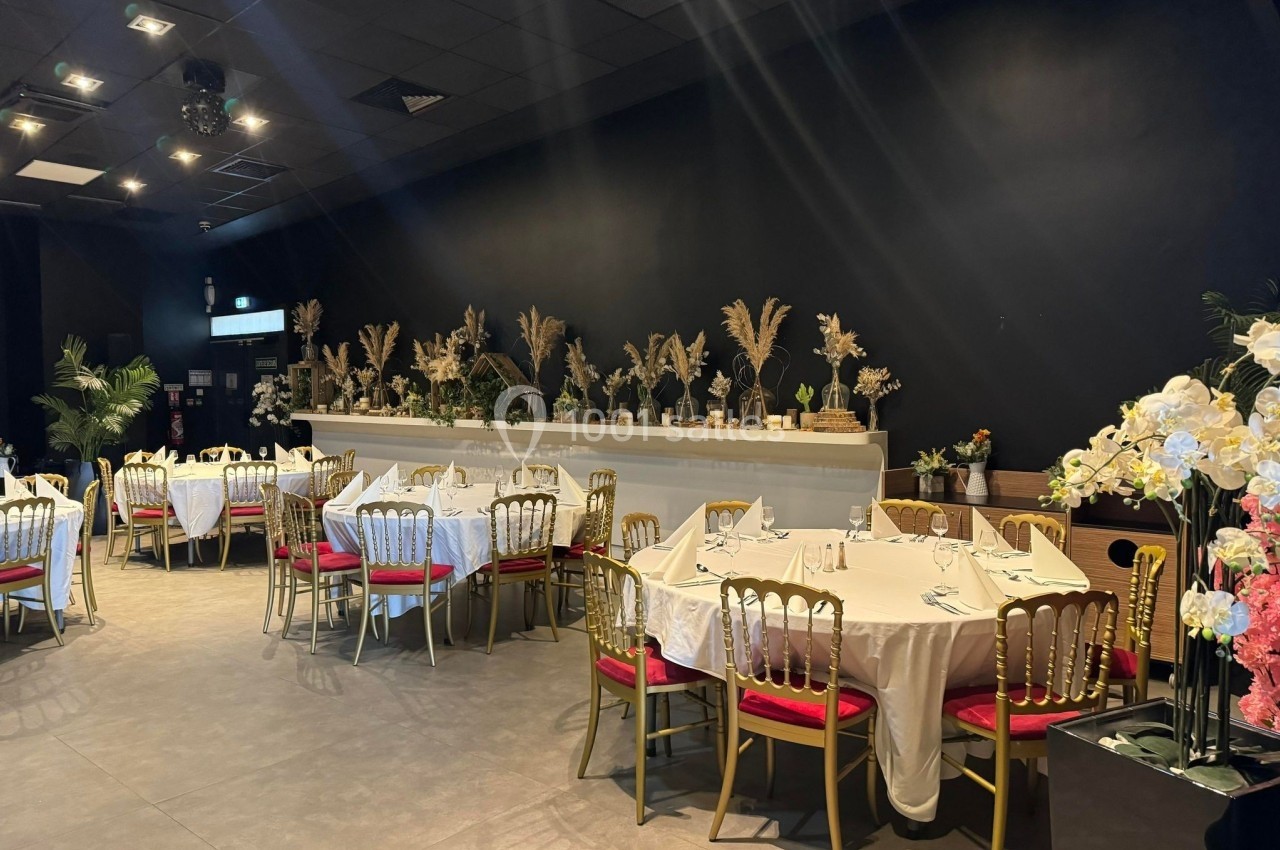 Salle de réception élégante avec tables rondes dressées, chaises dorées et décoration florale sur un fond sombre.