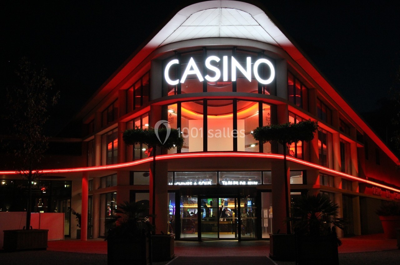 Façade d'un casino éclairée par des néons rouges et blancs, avec des plantes en premier plan, de nuit.