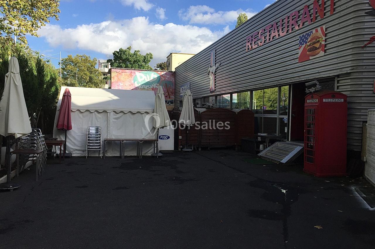 Terrasse extérieure d'un restaurant avec parasols fermés, chaises empilées et cabine téléphonique rouge.