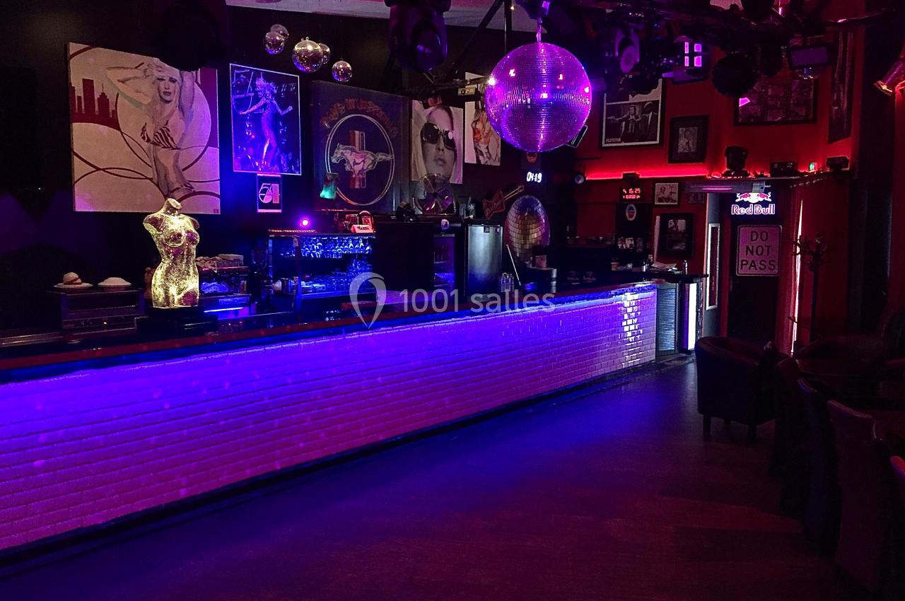 Bar avec comptoir éclairé en bleu, décorations murales artistiques, boule disco suspendue et ambiance tamisée.