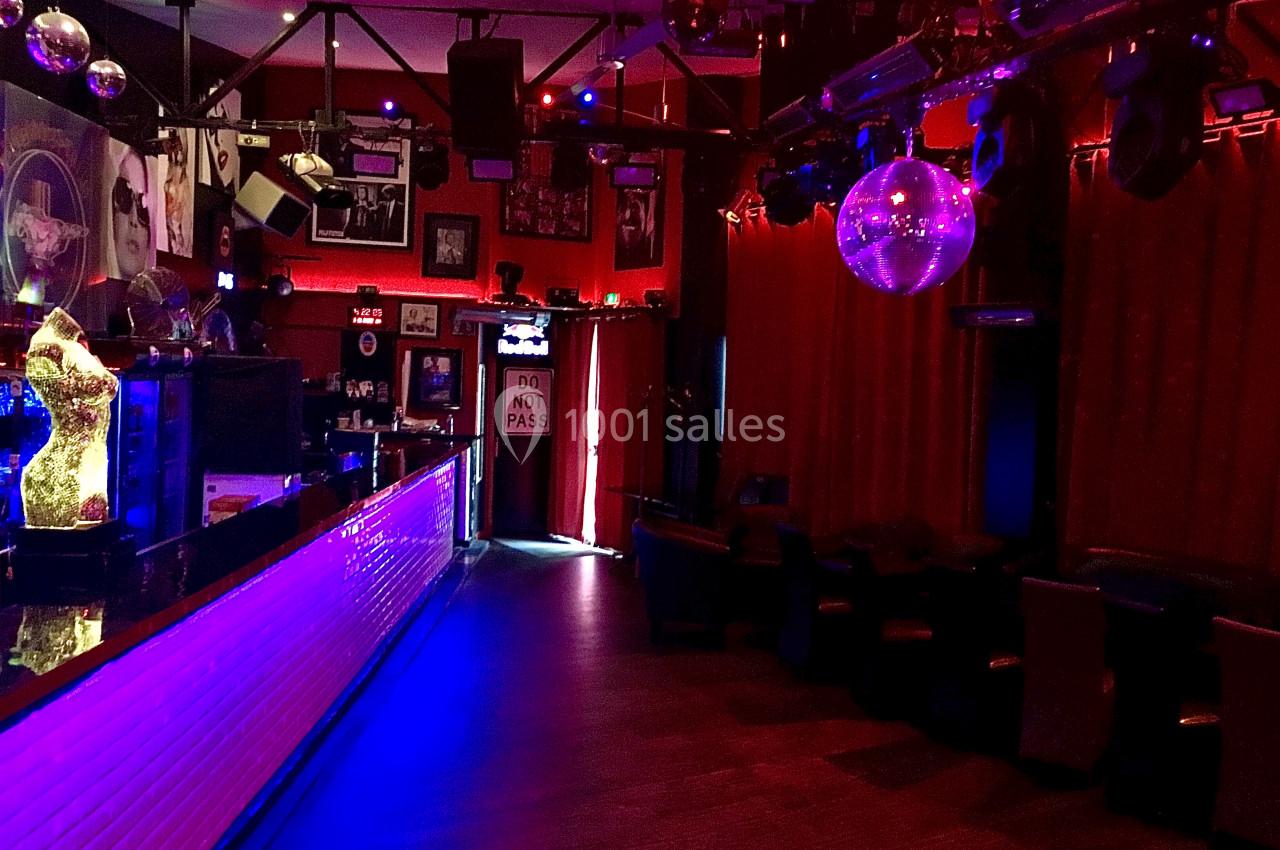 Intérieur d'un bar ou d'une discothèque avec éclairage tamisé, comptoir lumineux et boule disco suspendue.