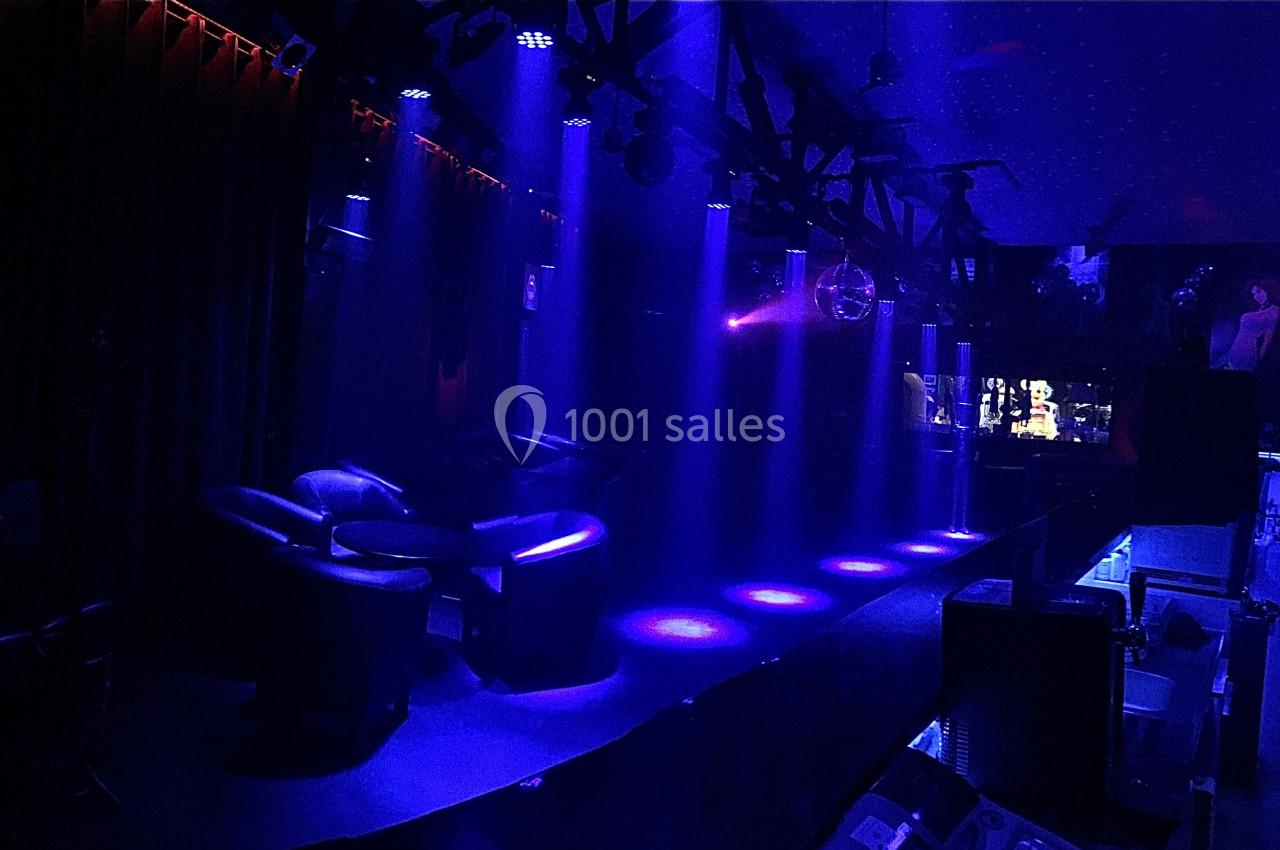 Salle sombre avec fauteuils, éclairée par des projecteurs bleus et une boule à facettes suspendue au plafond.