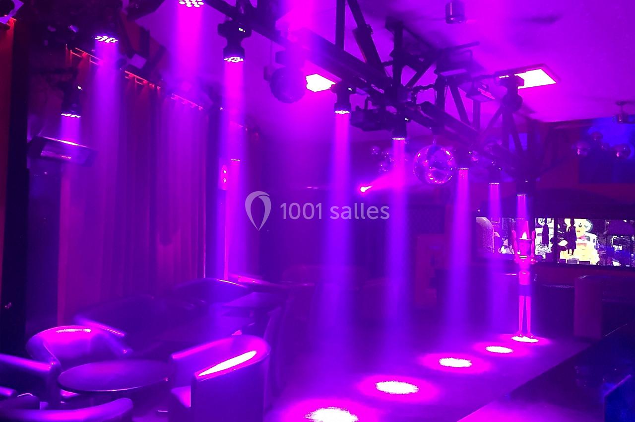 Salle sombre avec des fauteuils, éclairée par des projecteurs violets et une boule disco suspendue.