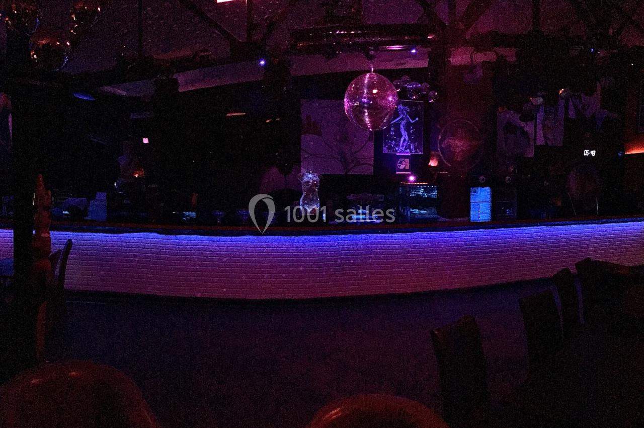 Comptoir de bar éclairé par des lumières violettes et bleues dans une ambiance sombre de club ou de discothèque.