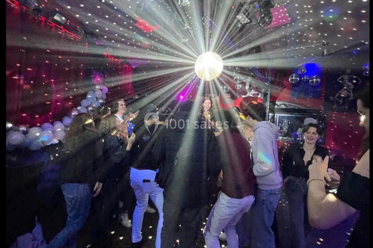 Des personnes dansent sous une boule à facettes dans une salle éclairée par des lumières colorées et des spots.