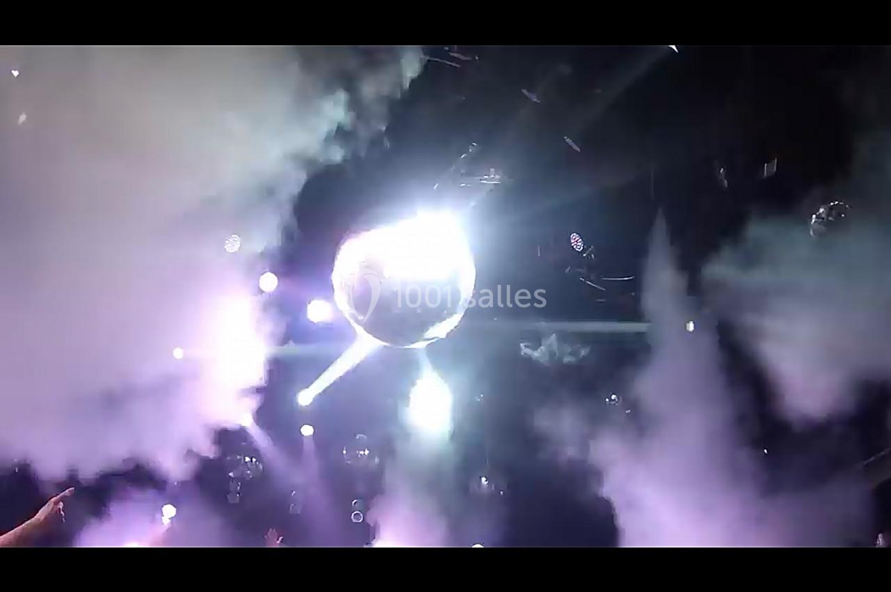 Boule disco suspendue au plafond, entourée de fumée et éclairée par des projecteurs dans une ambiance festive.