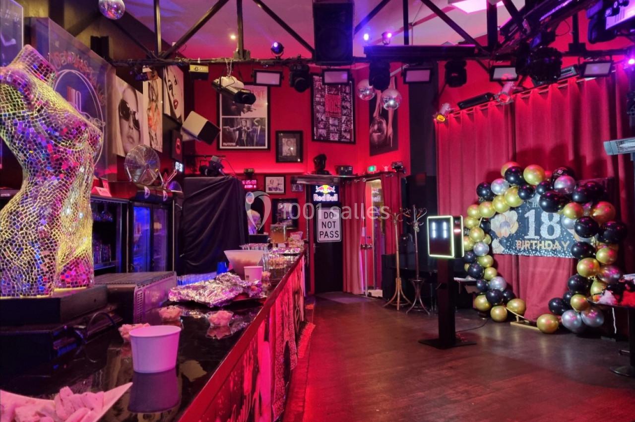Salle décorée pour un 18e anniversaire avec ballons dorés et noirs, buffet sur un comptoir et éclairage coloré.