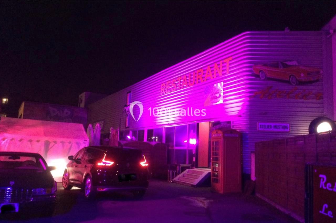 Façade d'un restaurant éclairée en violet avec des voitures anciennes garées devant et une cabine téléphonique rouge.