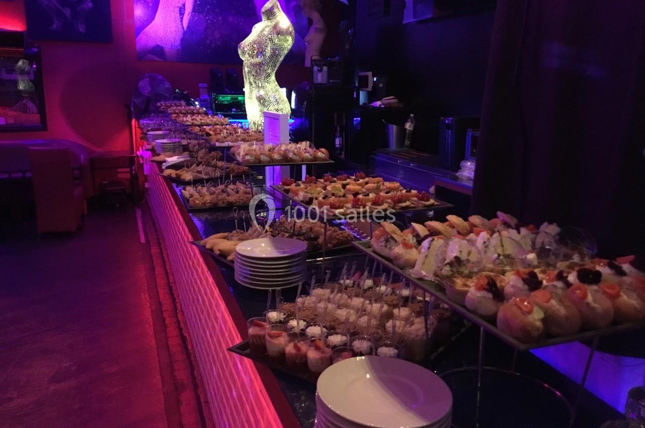 Buffet de cocktails et amuse-bouches variés disposés sur des étagères dans une salle à l'éclairage tamisé.