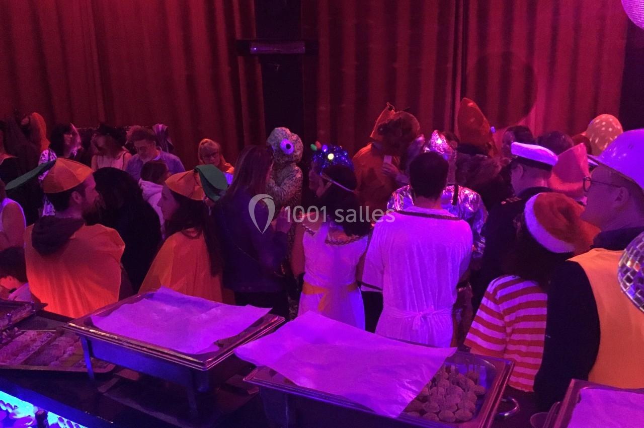 Personnes déguisées rassemblées dans une salle sombre avec des buffets éclairés par une lumière violette.