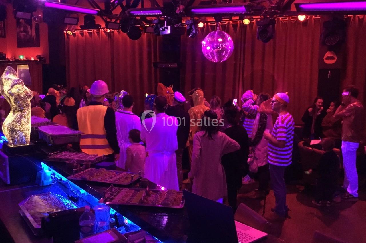 Groupe de personnes déguisées lors d'une fête dans une salle éclairée par des lumières colorées et une boule disco.