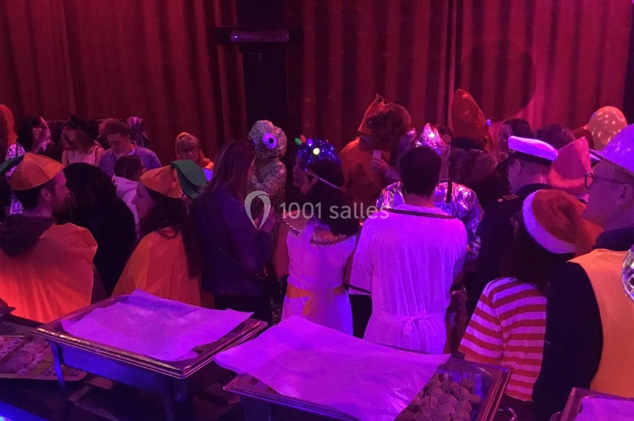 Groupe de personnes déguisées lors d'une fête, rassemblées près d'un buffet dans une salle éclairée par des lumières rouges.