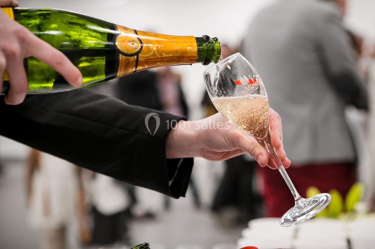 Une main verse du champagne dans une flûte lors d'un événement, avec un arrière-plan flou.