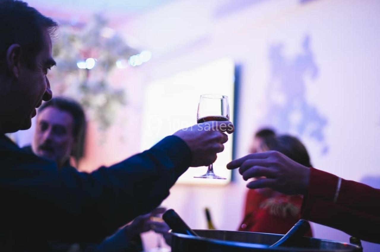 Une personne tend un verre de vin à une autre dans un cadre festif avec une lumière tamisée.