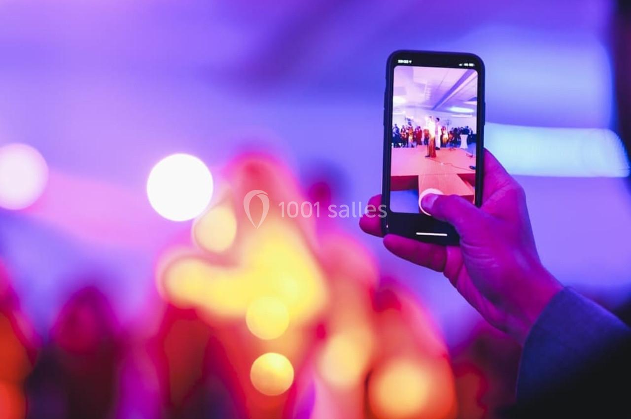 Une personne filme une scène lumineuse et floue avec un smartphone dans un environnement coloré.