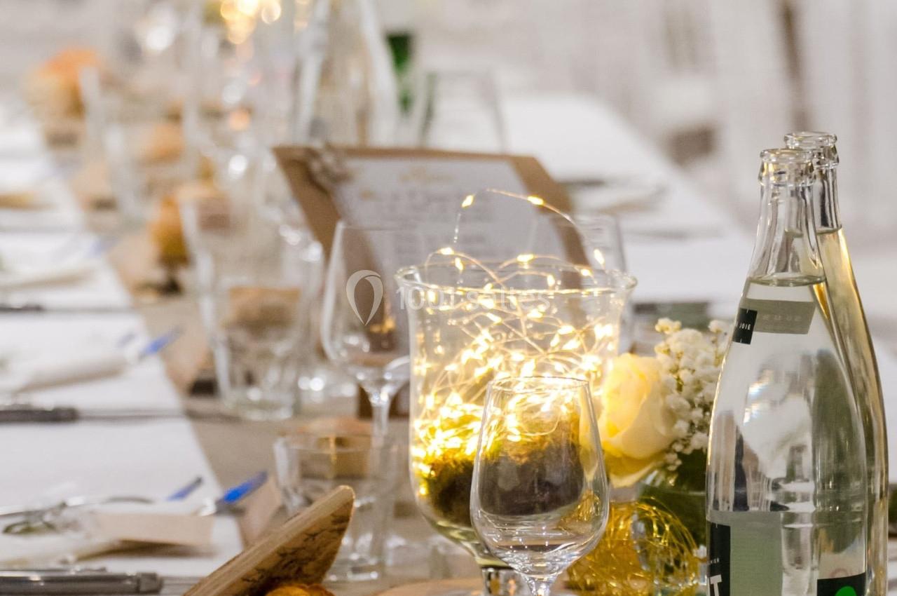 Table décorée pour un événement avec guirlandes lumineuses, verres, bouteilles d'eau et fleurs blanches.