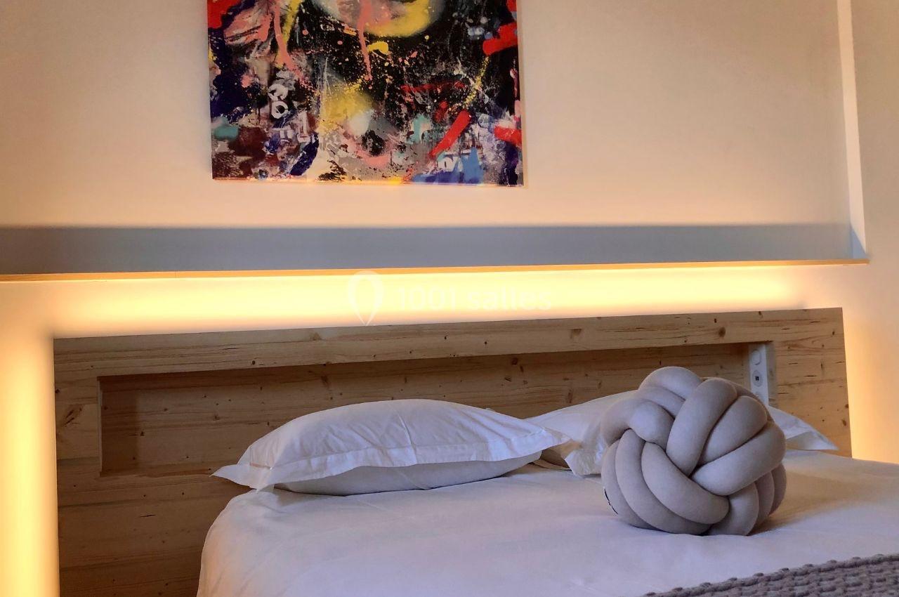 Lit avec tête de lit en bois éclairée, coussins blancs et décoration murale colorée en arrière-plan.