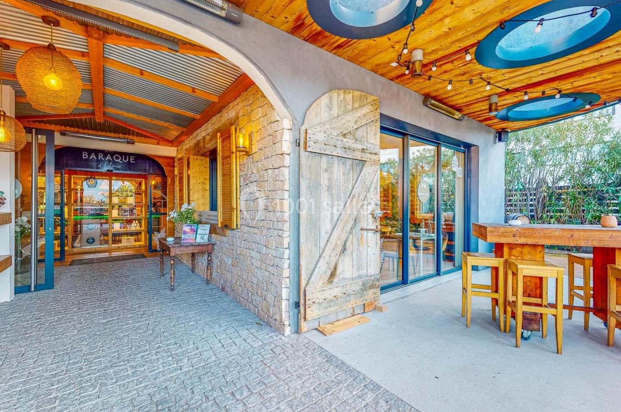 Entrée d'un restaurant avec porte en bois, terrasse couverte, tables hautes et décoration chaleureuse.