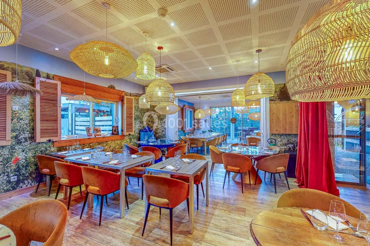 Salle de restaurant lumineuse avec tables en bois, chaises rembourrées et luminaires suspendus en osier.
