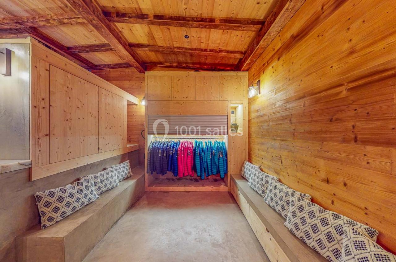 Vestiaire en bois avec bancs rembourrés et rangée de vestes colorées suspendues au fond.