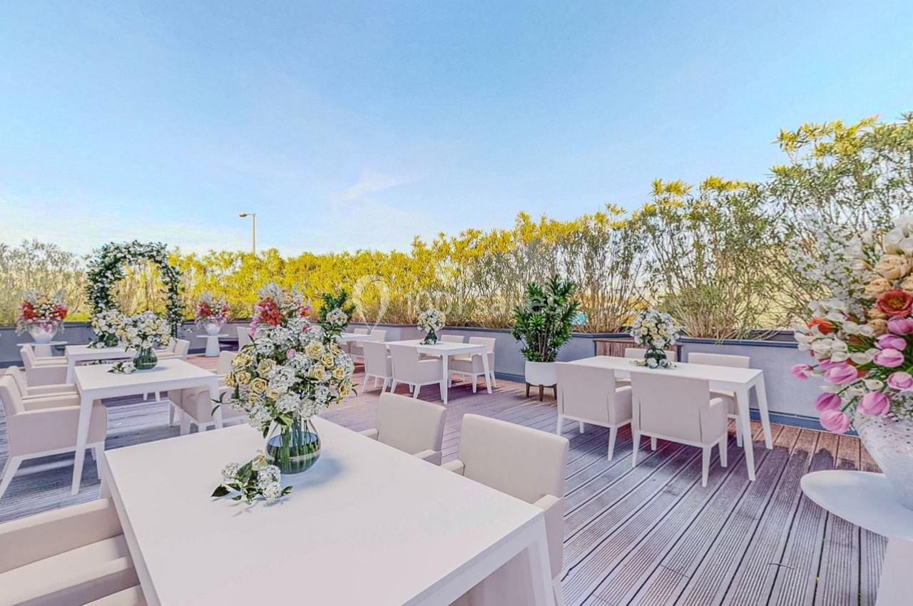 Terrasse aménagée avec des tables blanches, des chaises et des compositions florales, entourée de végétation.