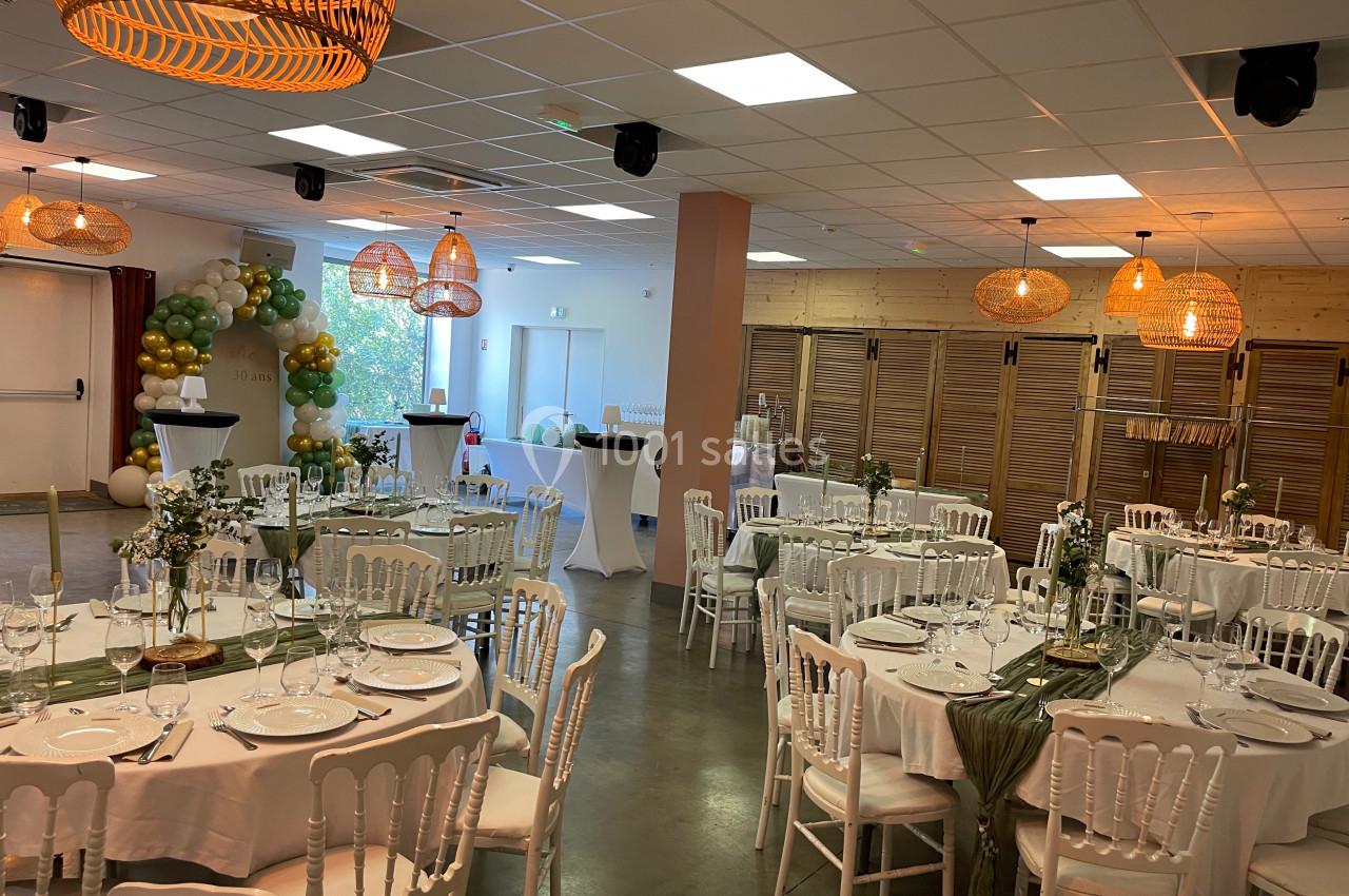 Salle de réception décorée avec des tables dressées, des chaises blanches, des guirlandes de ballons et des luminaires…