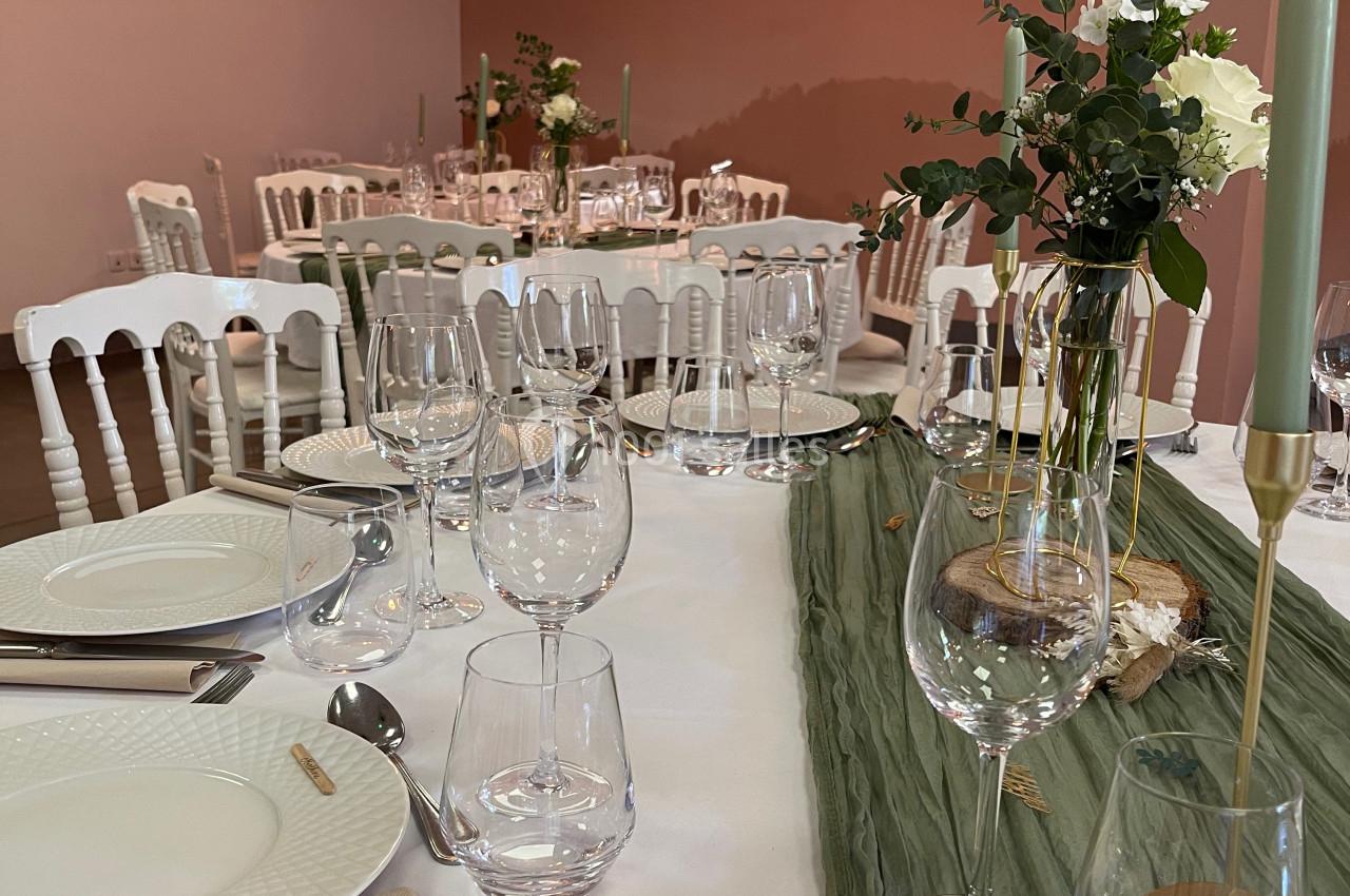 Table dressée avec vaisselle blanche, verres et bougies, décorée de fleurs et d'un chemin de table vert dans une salle…