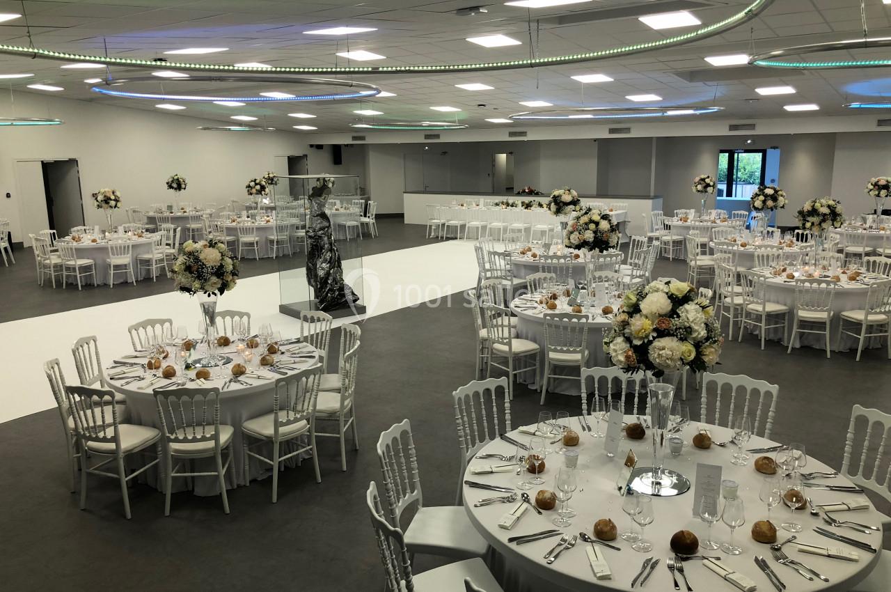 Salle de réception élégante avec tables rondes dressées, décorations florales et éclairage moderne.